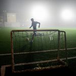 man in black shirt standing on soccer goal net during night time